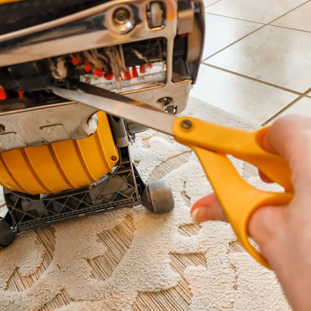 using scissors to cut away hair on the roller of the vacuum