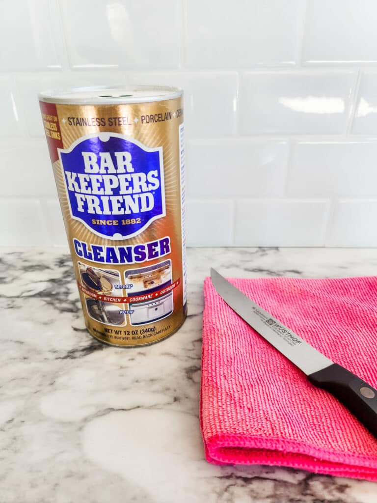 Bar keepers friend sitting next to a pink towel with a knife on top.