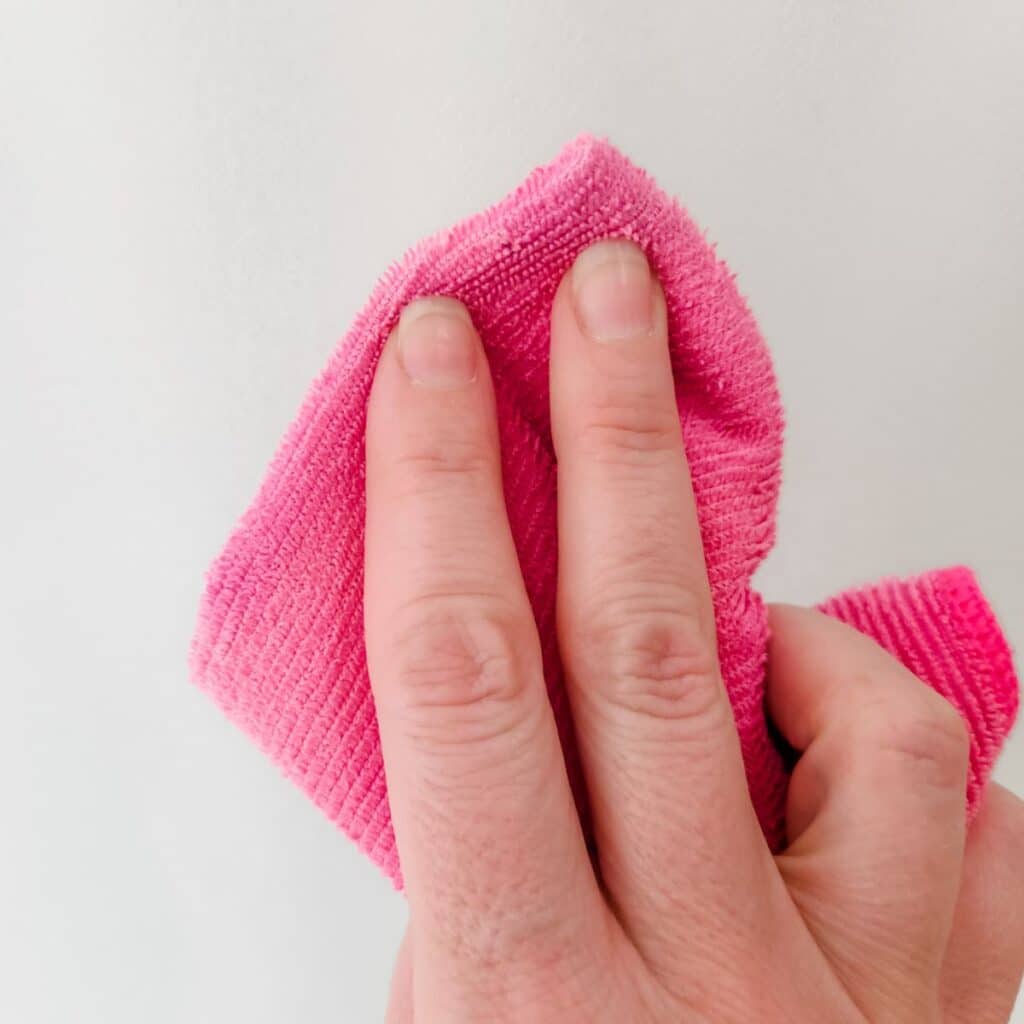 Removing soap scum from a shower door with bar keepers friend and pink towel.