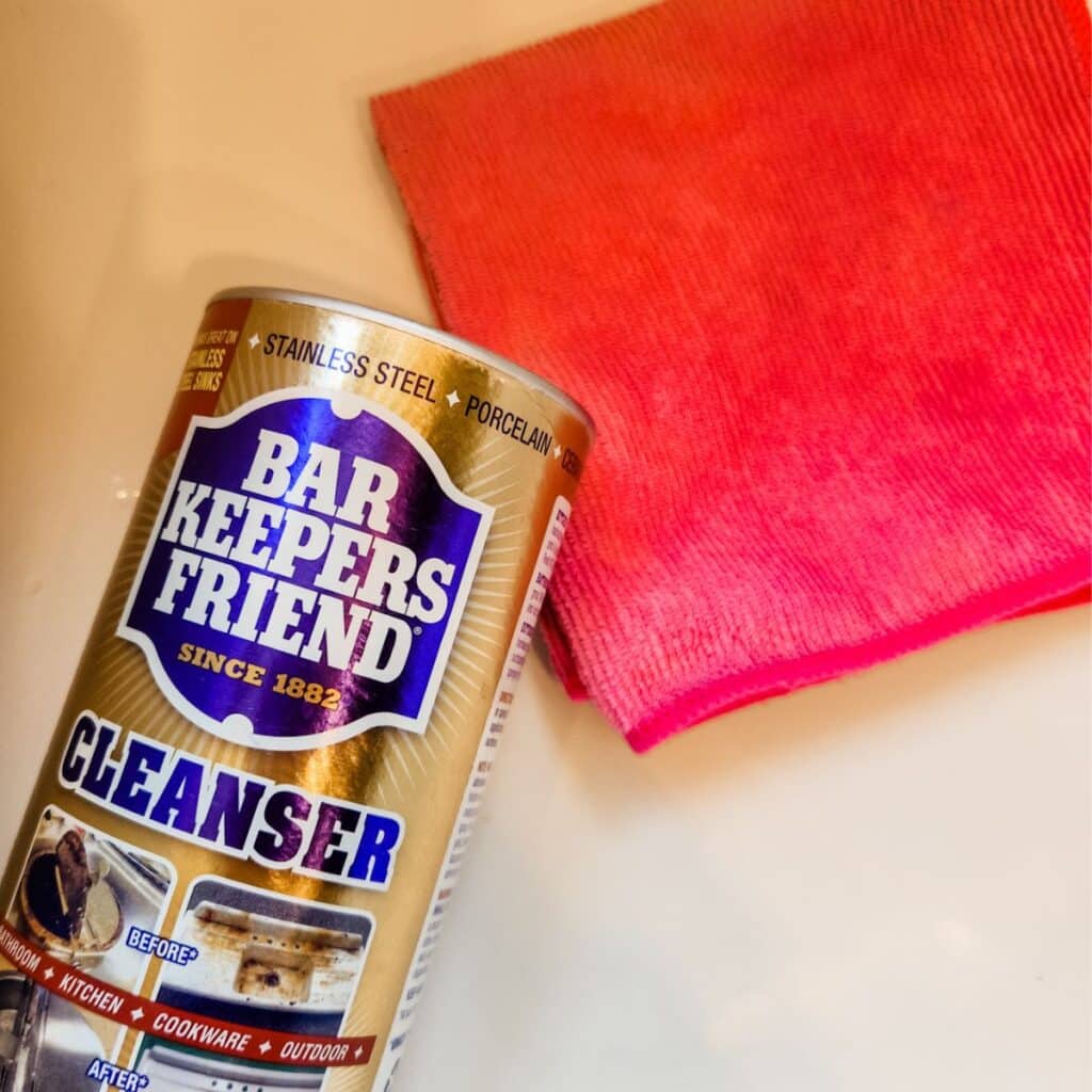 Bar keepers friend laying in the sink with a pink cloth.